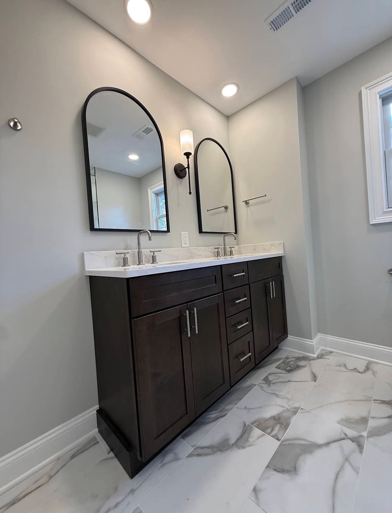 Dark wood vanity with twin arched mirrors and marble tile floor