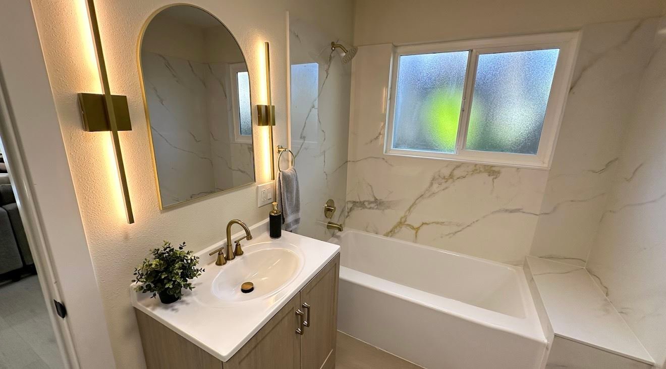 Marble bathroom remodel with arched brass-trimmed mirror, gold sconces, and custom tile shower