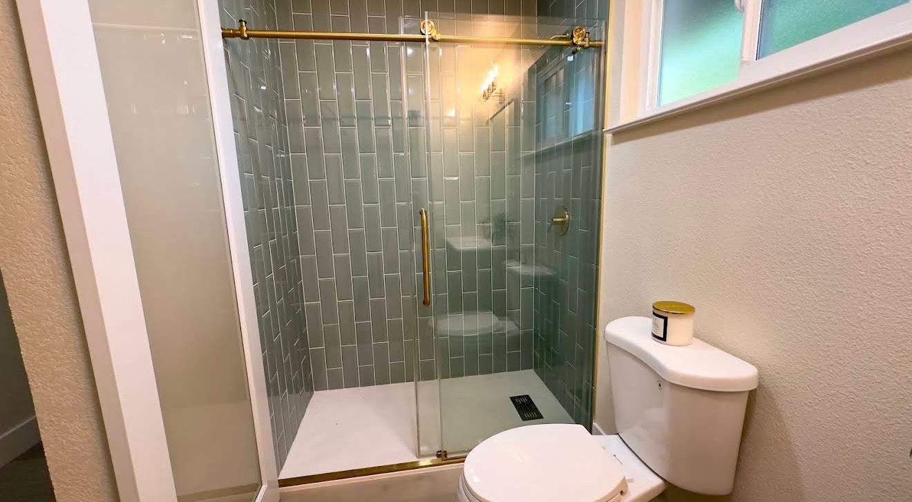 Custom vertical teal subway tile shower with brass gold hardware and rain head, installed in a Portland-area bathroom